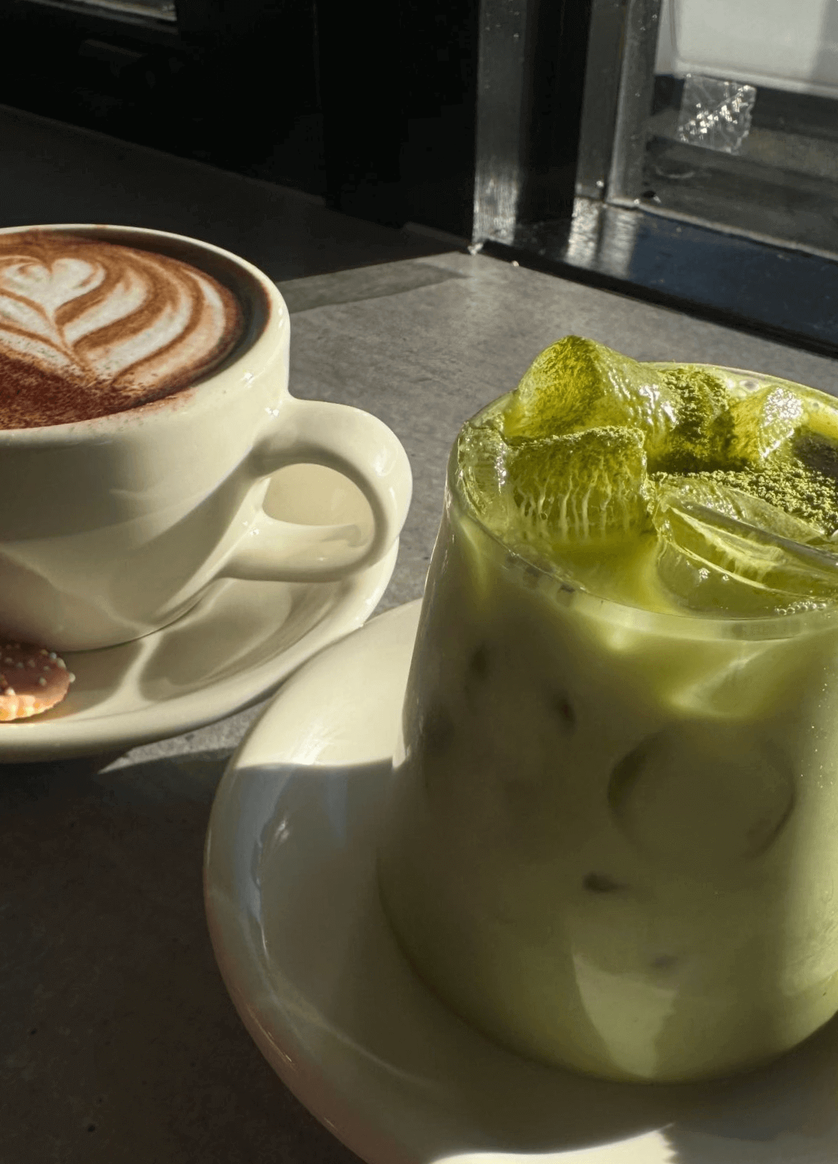 An iced glass of matcha and a white mug with a cappucino